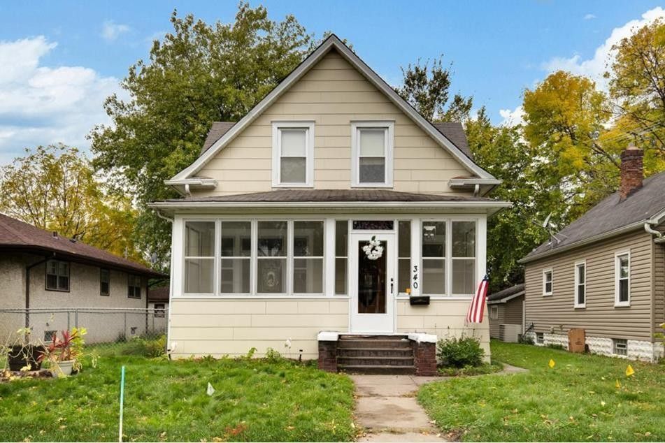 Beige house with porch and American flag; sunny day.