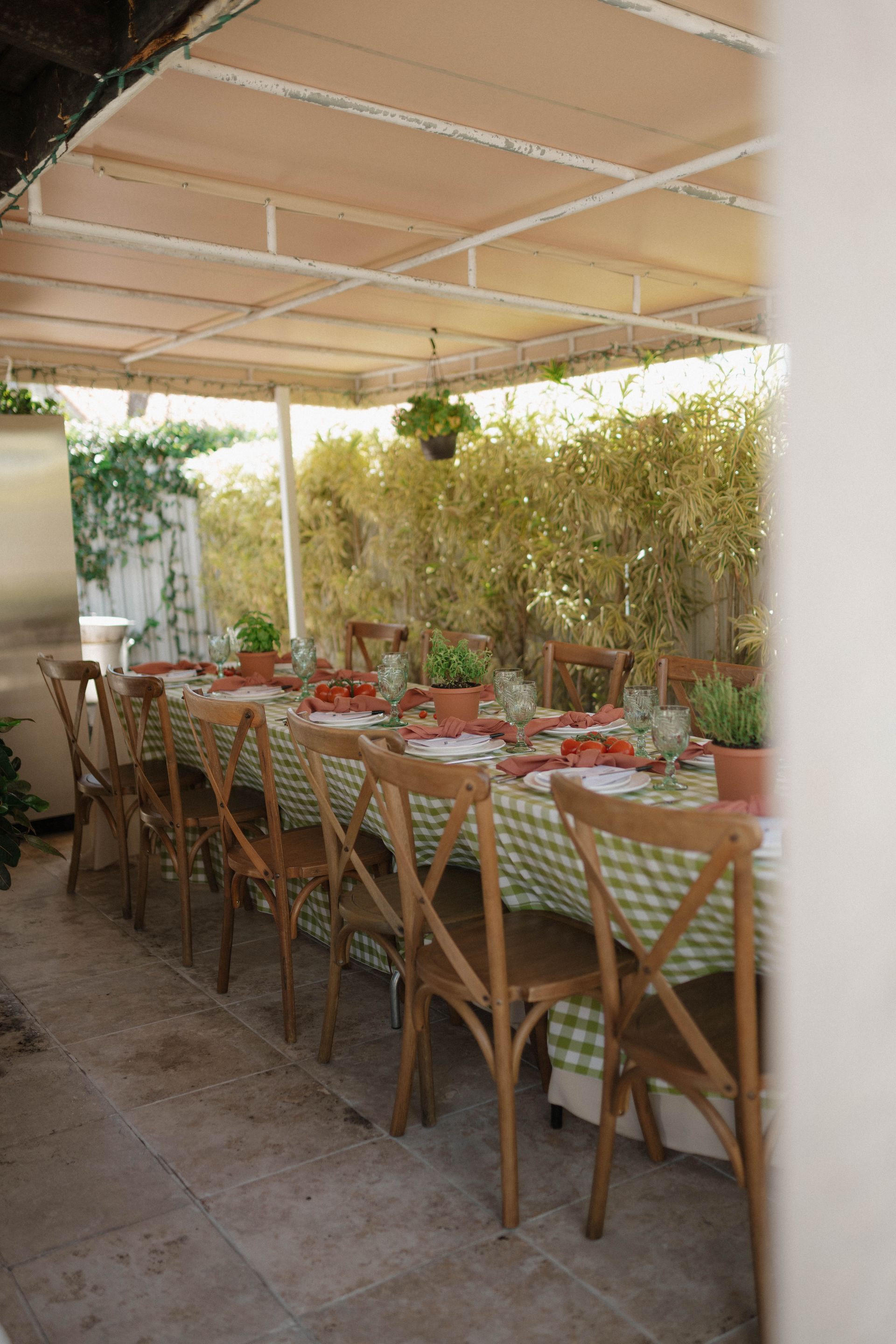 A long table with a checkered tablecloth and chairs under a canopy.