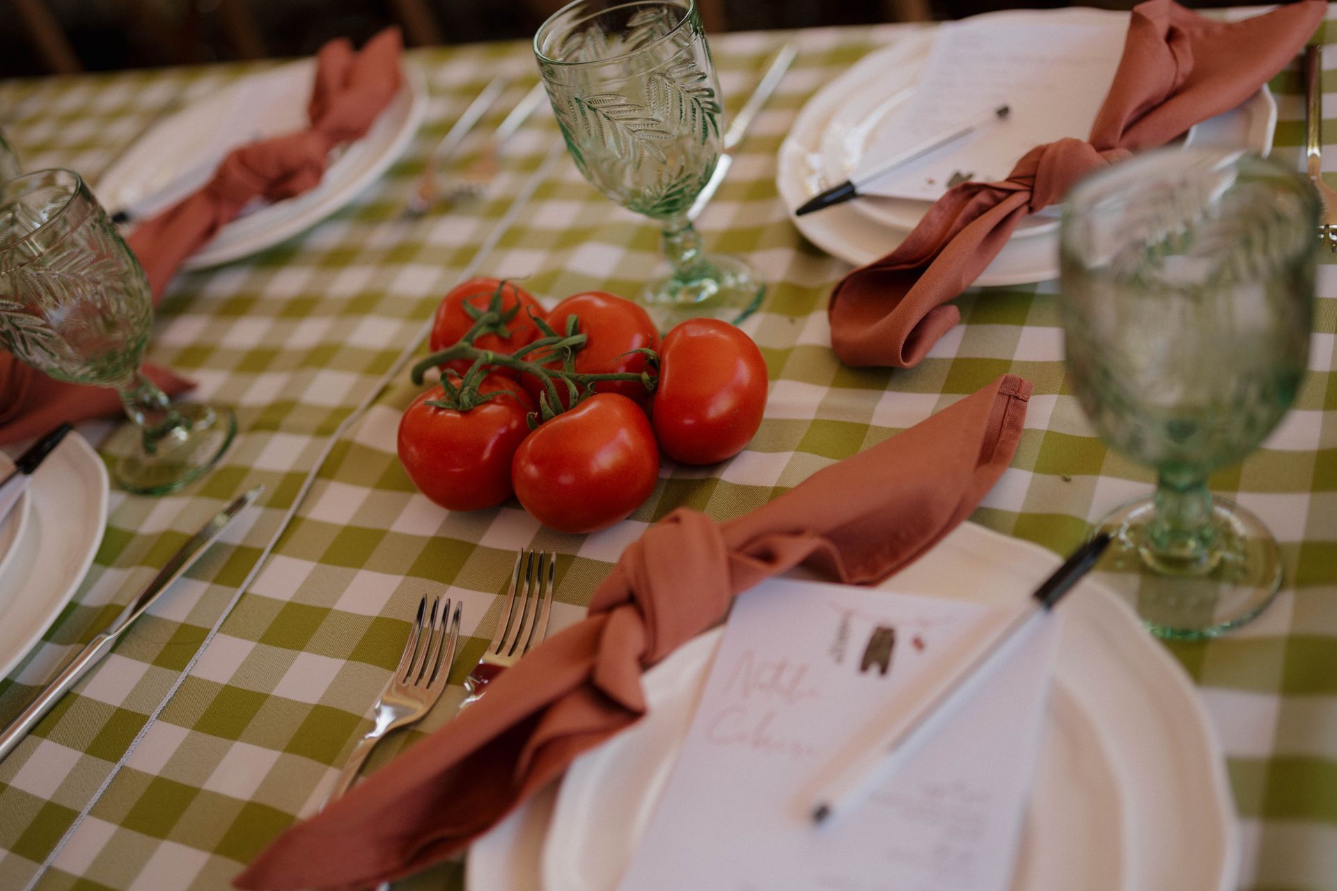 A table with plates, glasses, napkins and tomatoes on it.