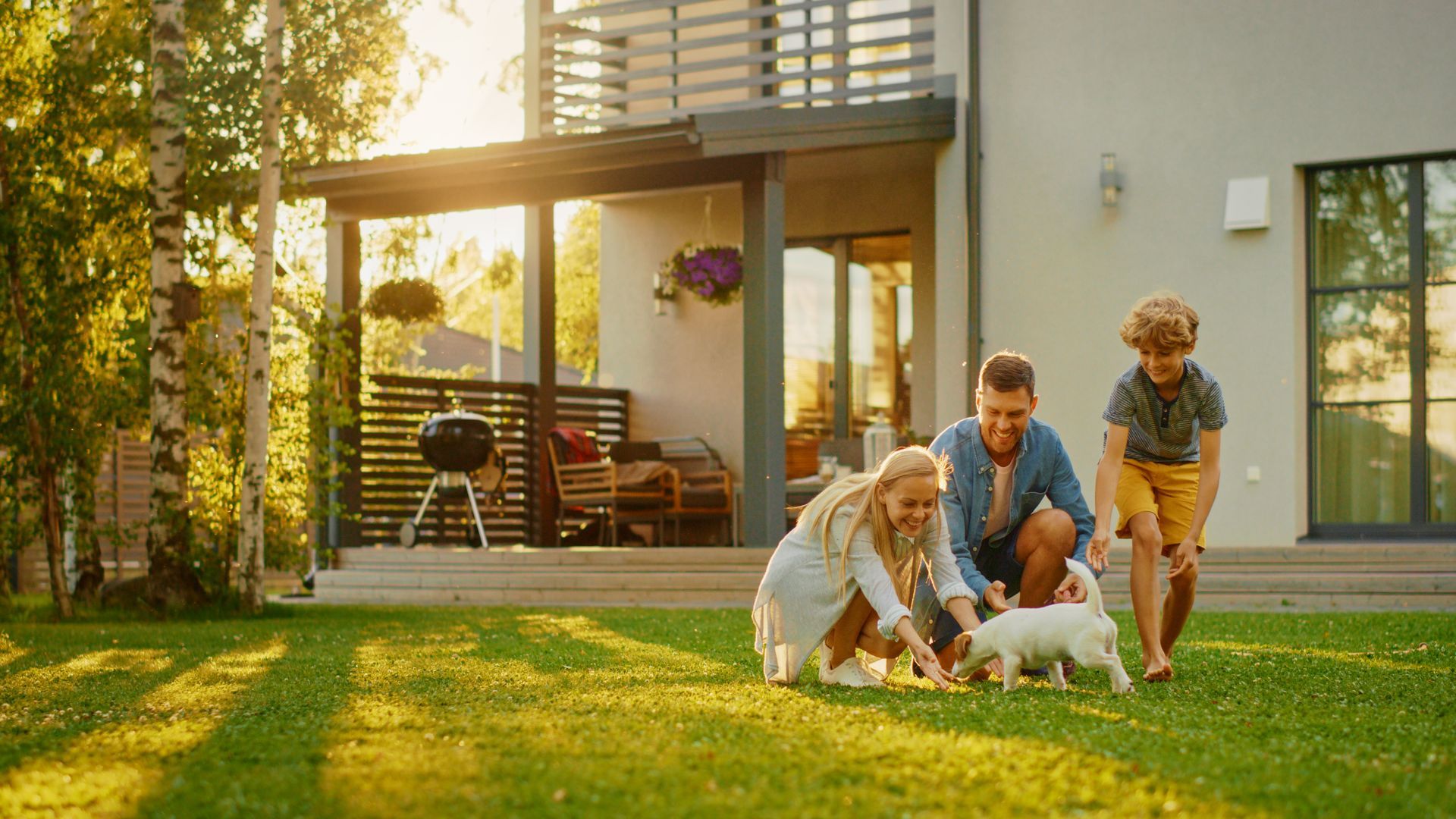 Family playing with a small white dog in their sunny backyard near their house.