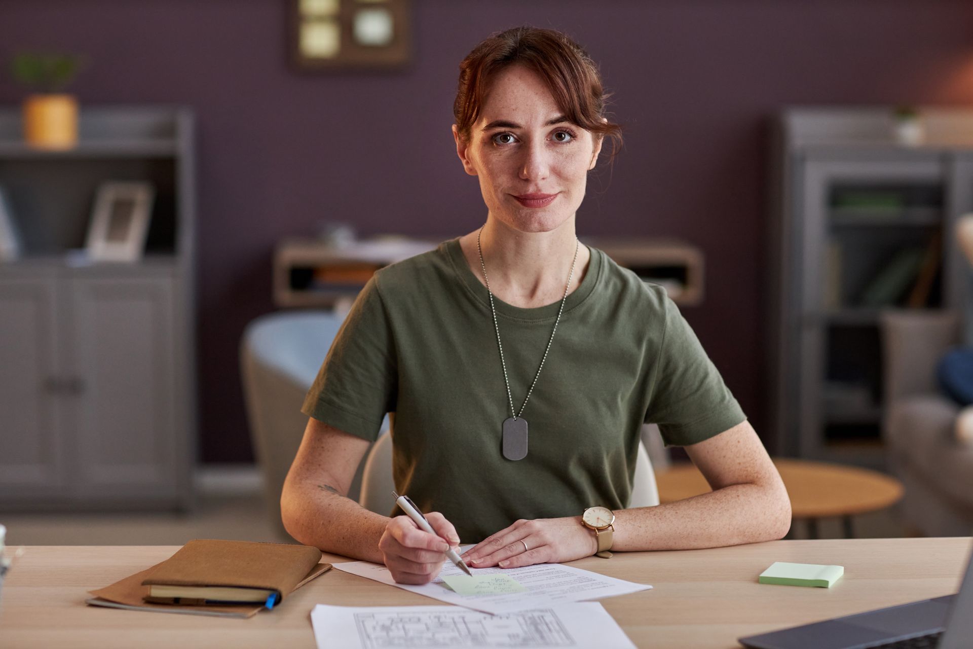 Portrait of woman wearing military uniform working at desk in office and looking at camera.