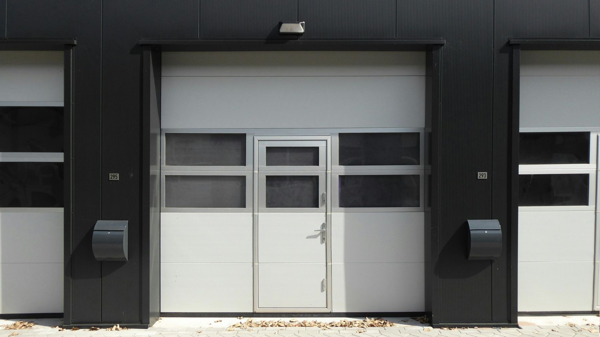 Garage door with an integrated pedestrian door, flanked by black pillars and white walls.