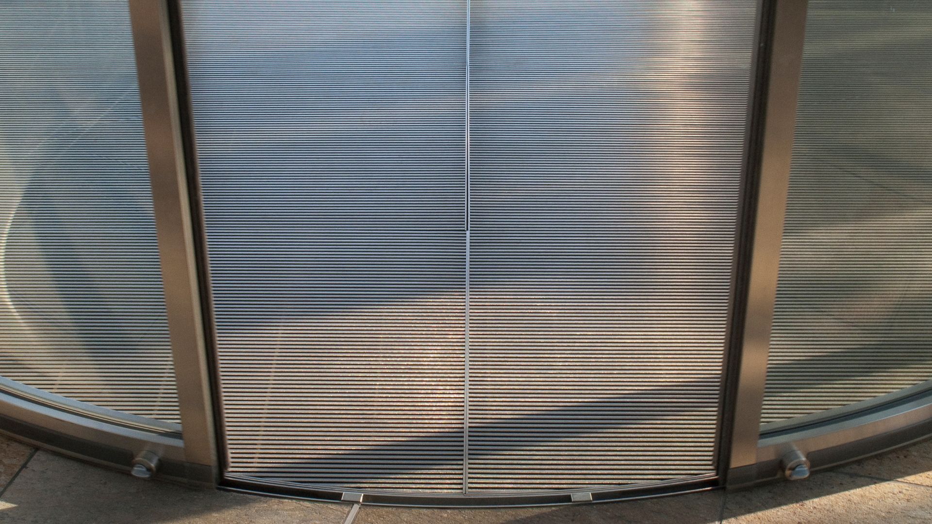 Metal-framed glass door with horizontal textured panels. Sunlight casts shadows.