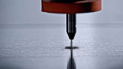 A close up of a screwdriver cutting a hole in a piece of metal.
