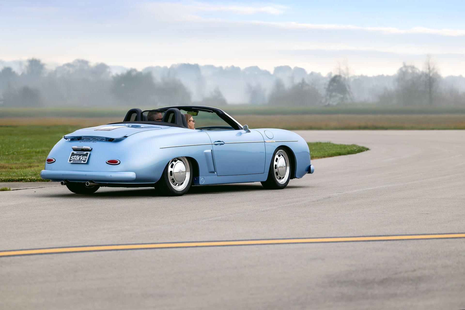 Light blue convertible sports car driving on an empty runway under a foggy sky