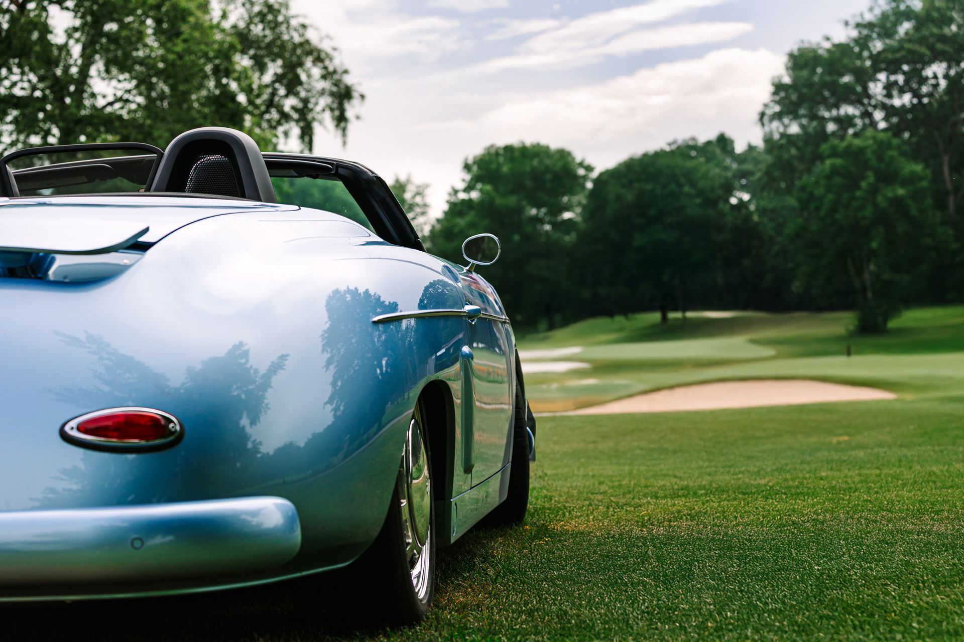 Blue vintage convertible parked on a golf course fairway near a sand bunker