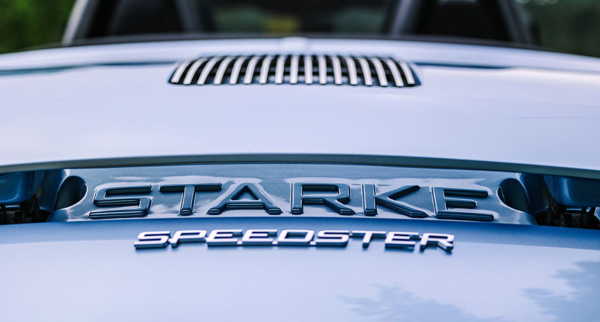 Close-up of a silver car hood badge reading “STARK SPEEDSTER” with a vent above it