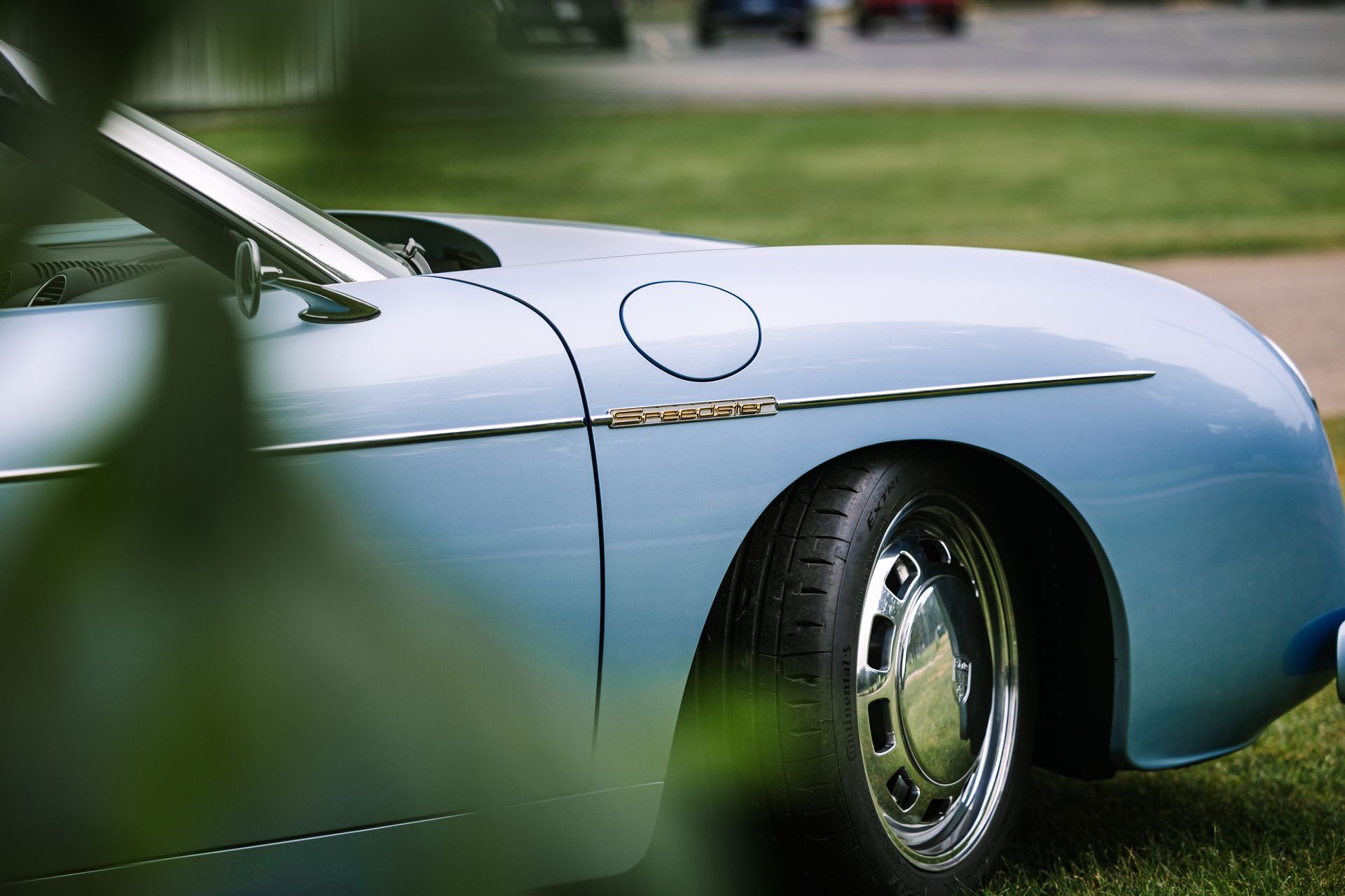 Light blue classic car parked on grass, showing side and rear wheel