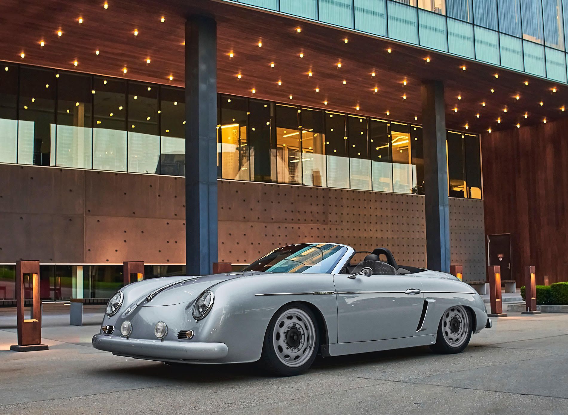 Silver classic convertible sports car parked outside a modern building at dusk