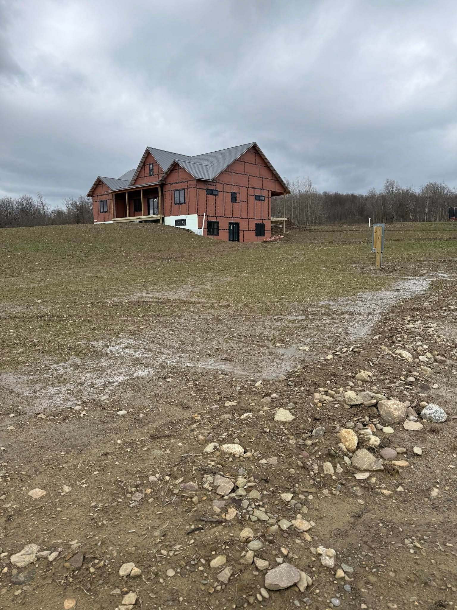 Red house on a grassy hill beside a rocky dirt path under an overcast sky