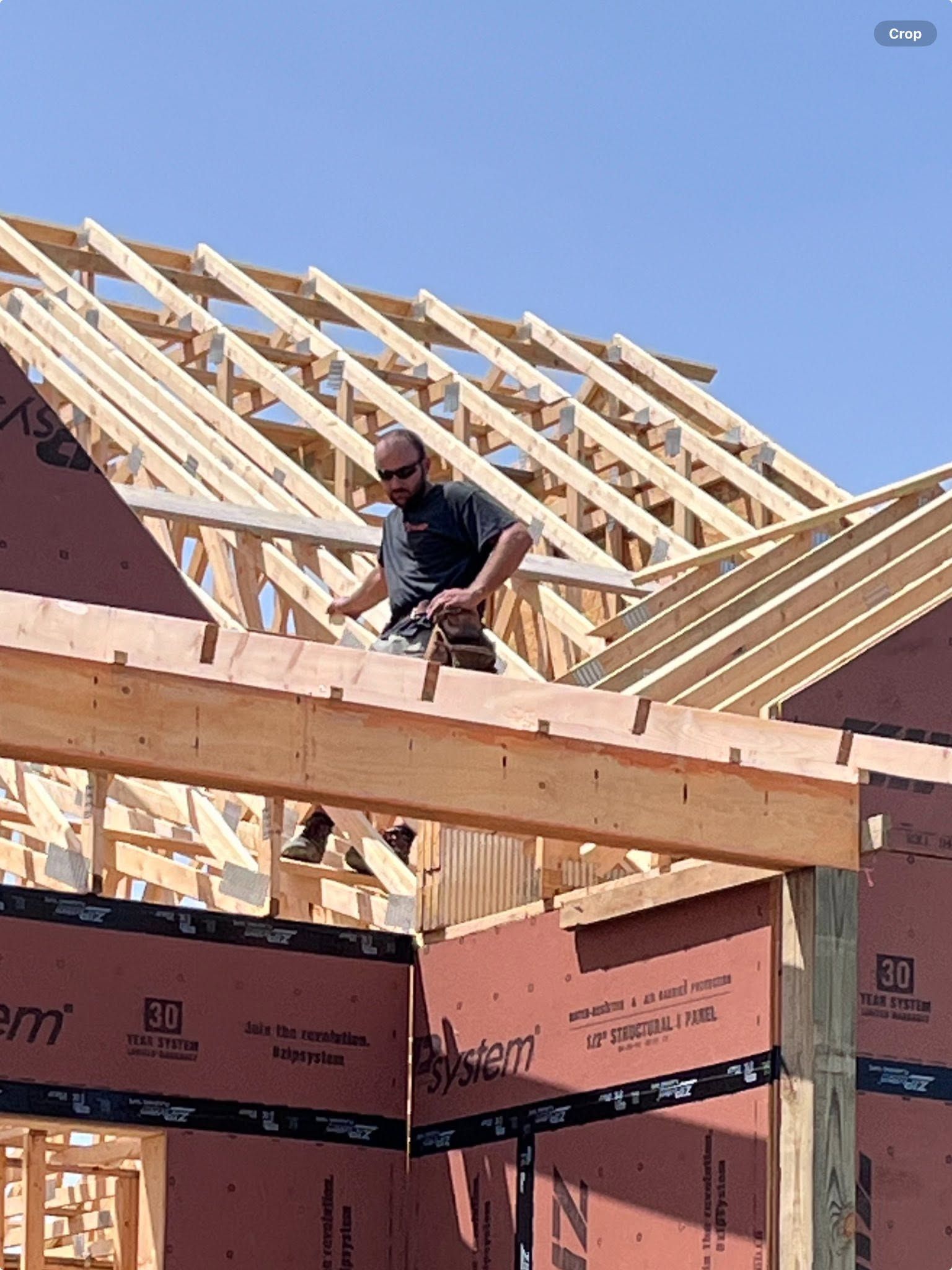 Worker on a roof frame at a house under construction against a blue sky.