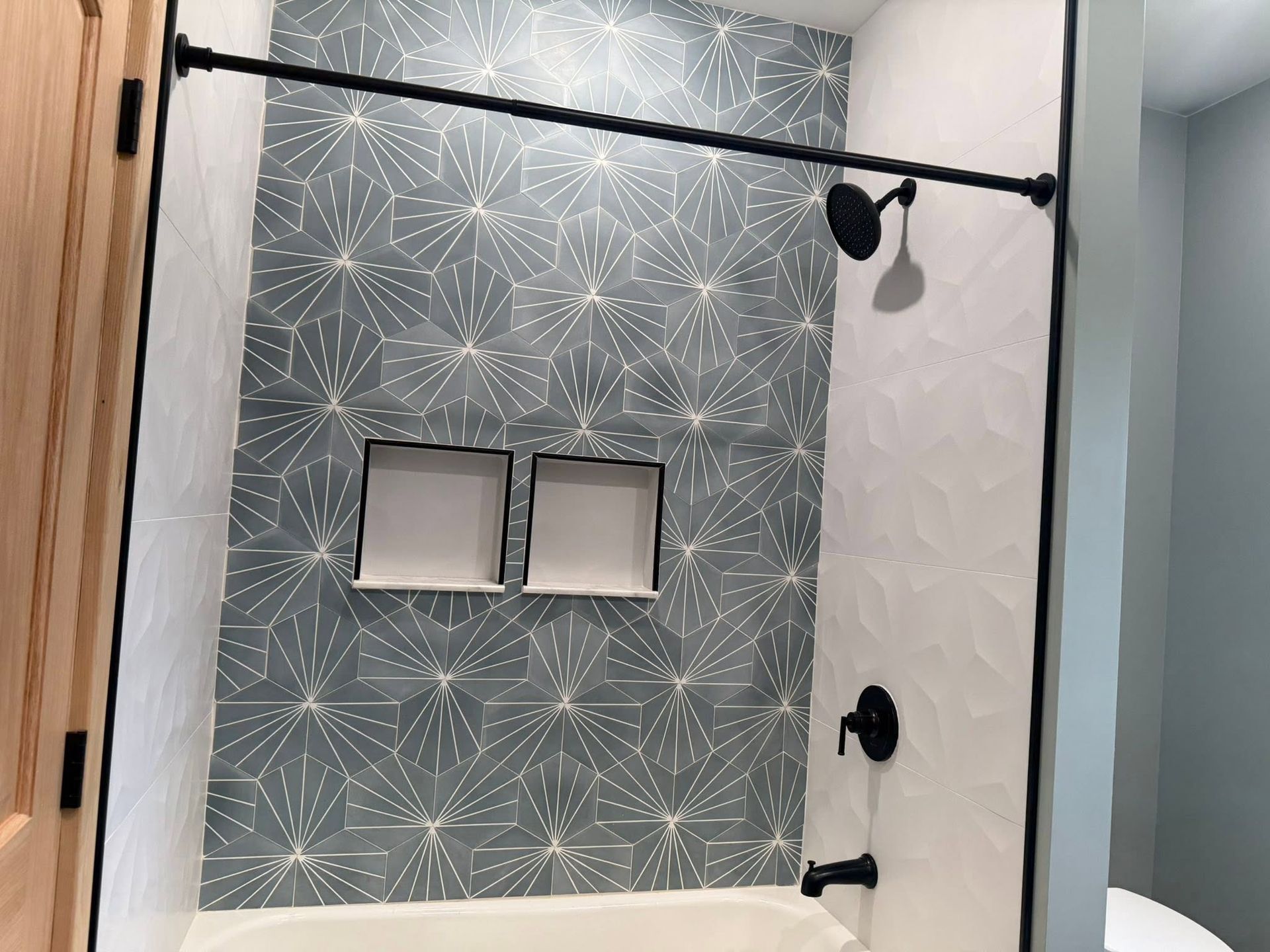 Bathroom shower with gray geometric tile, white side wall, and two recessed niches