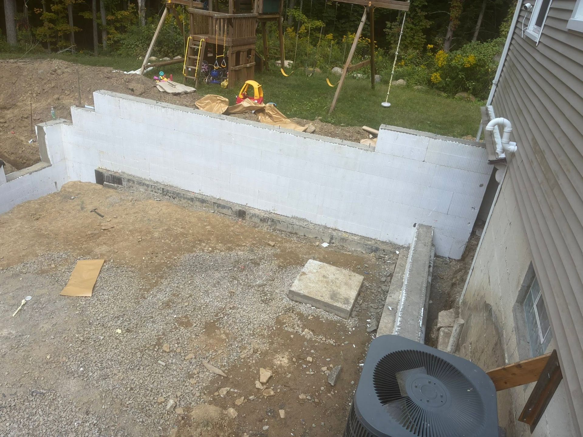 Backyard with a newly built white retaining wall, gravel ground, and construction materials near a house