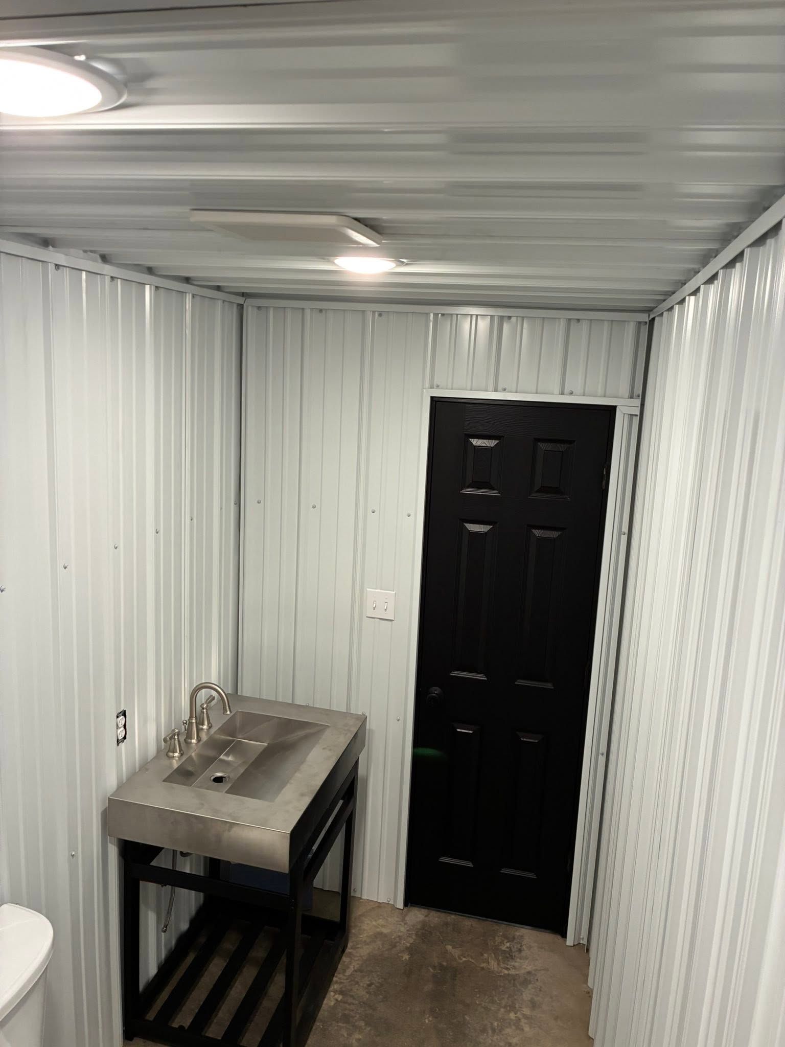 Small utility room with white paneled walls, sink, black door, and a wall light on the ceiling.