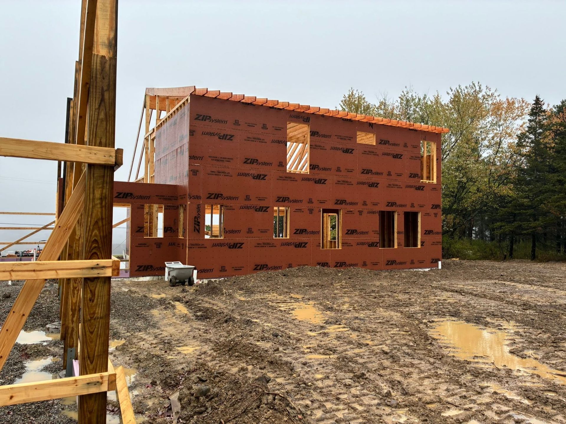 Partially built red house with wooden framing on a muddy construction site