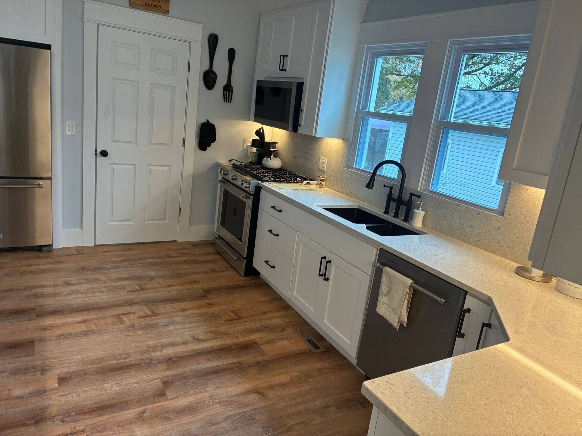Bright modern kitchen with white cabinets, wood floors, stainless appliances, and a window over the sink.
