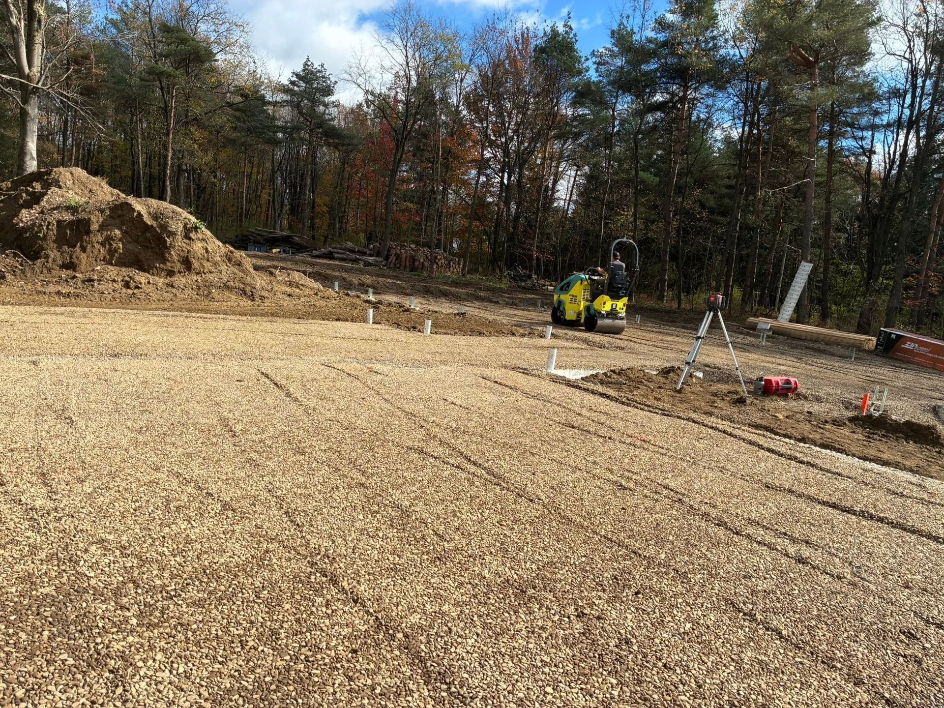 Construction site with workers in yellow vests on a gravel foundation beside a wooded area