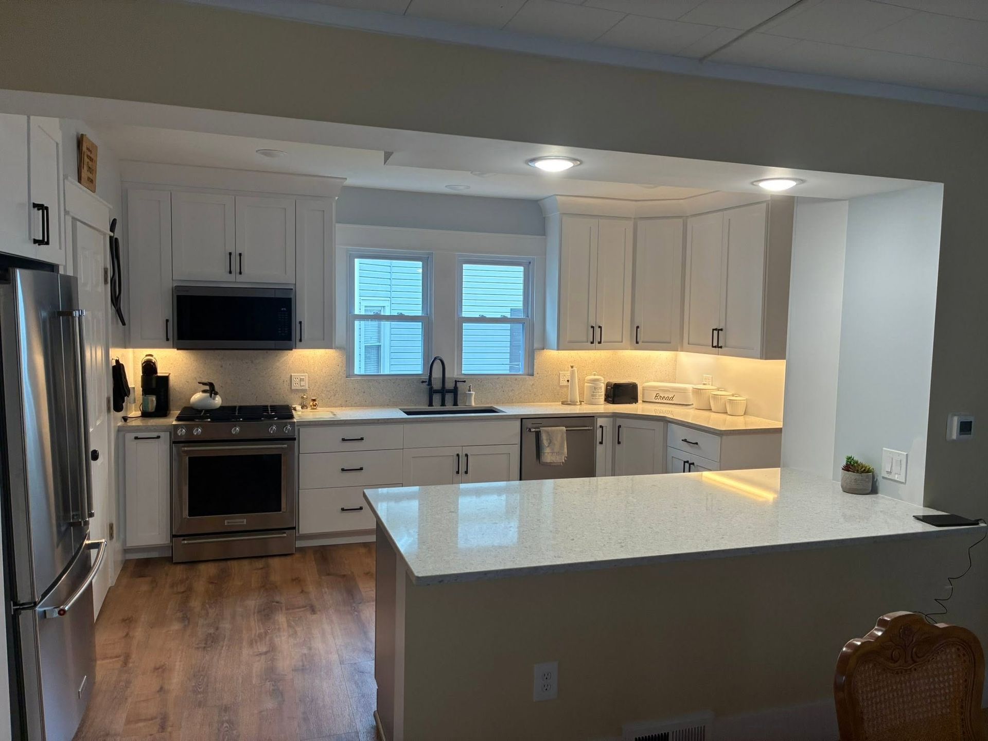 Bright, modern white kitchen with island, stainless appliances, and wood floors