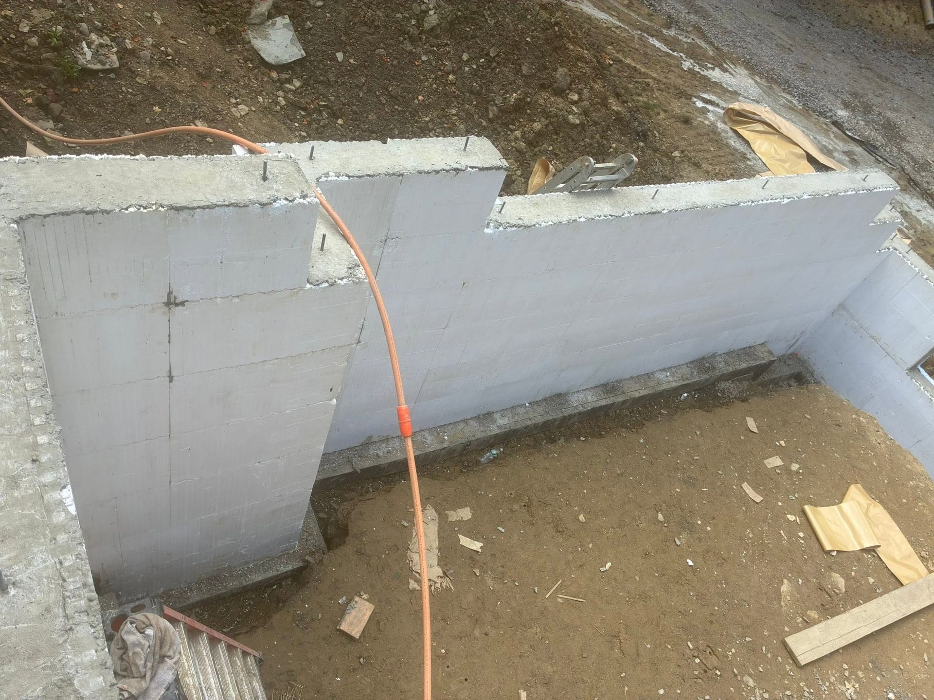 Concrete retaining wall under construction with an orange cord draped over the top, dirt yard in front.