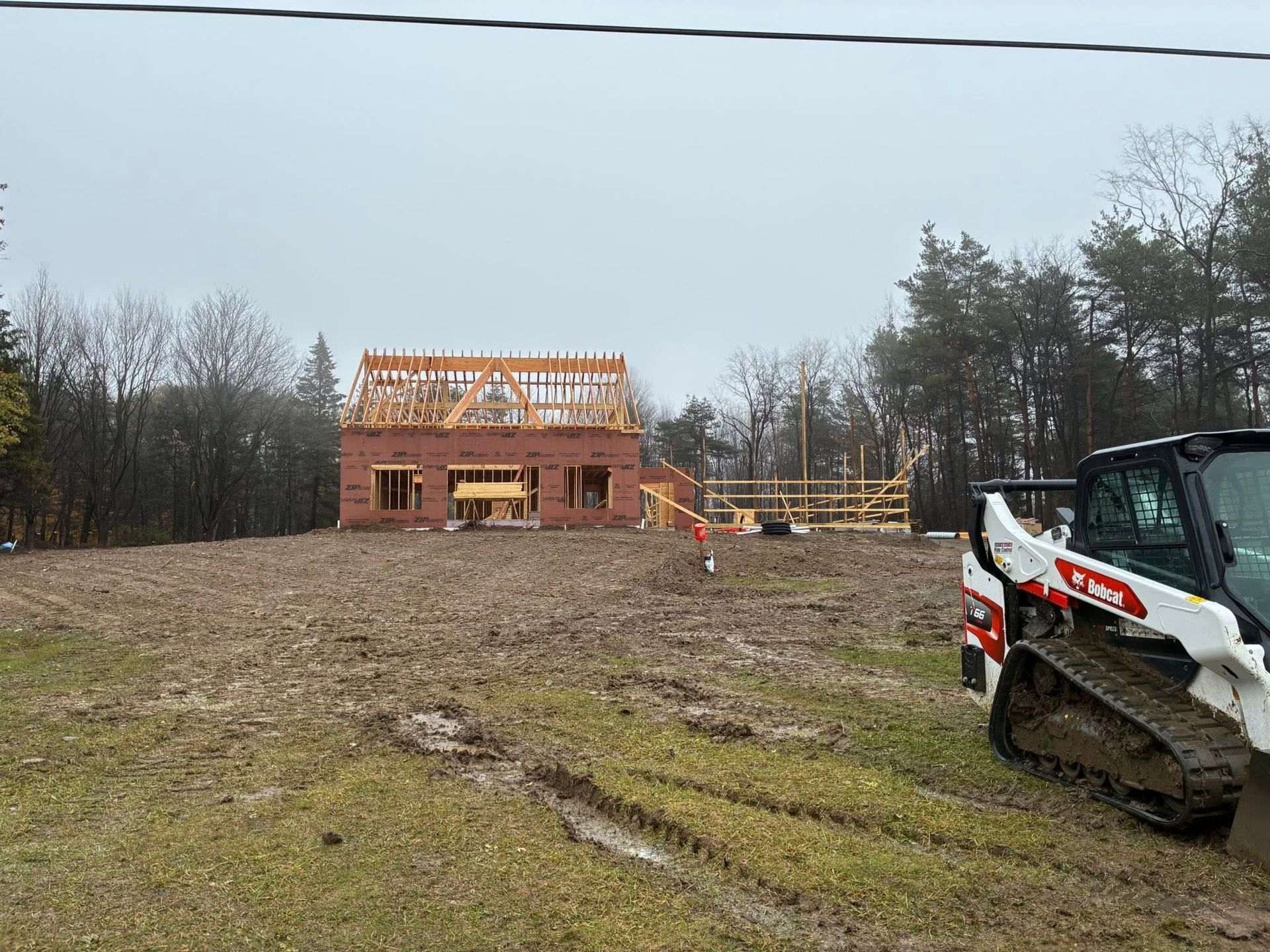 Construction site with a brick house under framing, muddy ground, and a compact loader on the right