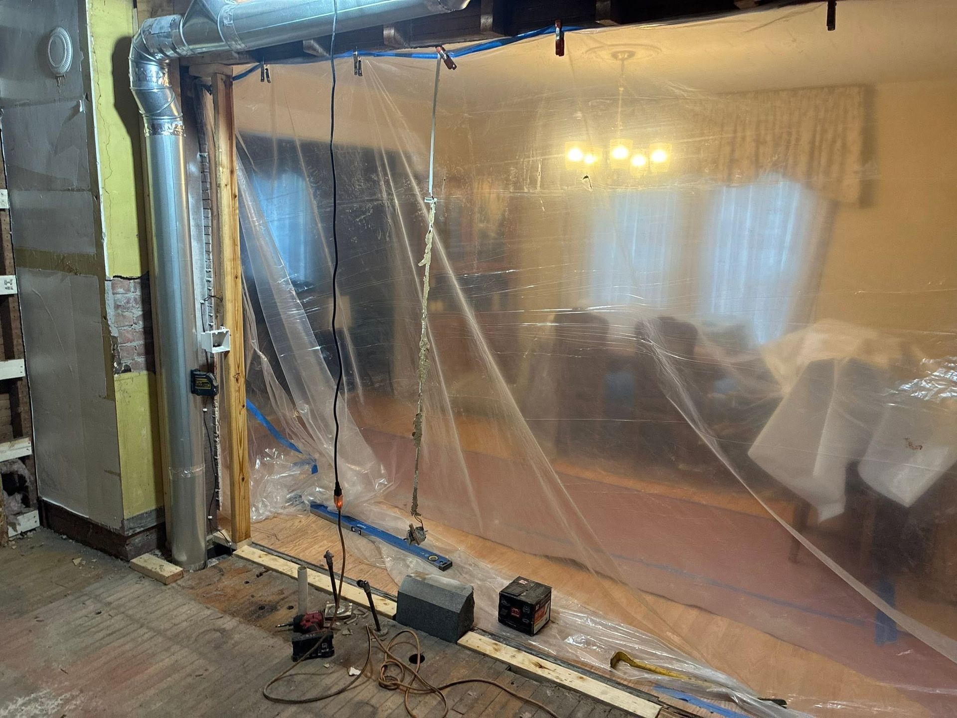 Renovation area with clear plastic sheeting over a wall and floor, tools and exposed ductwork visible