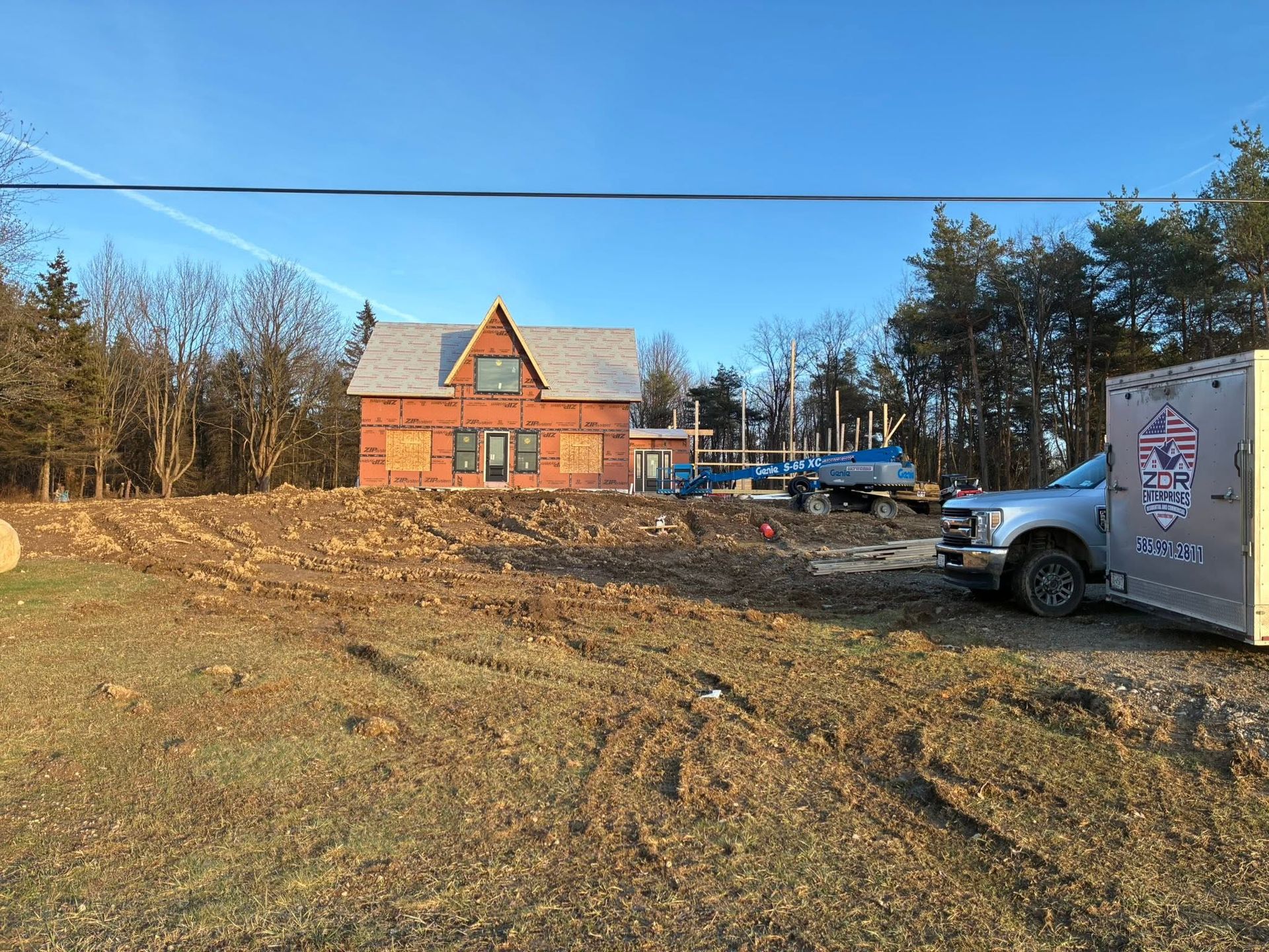 Rural lot with a red house under construction, trees in back, and a truck parked at right.