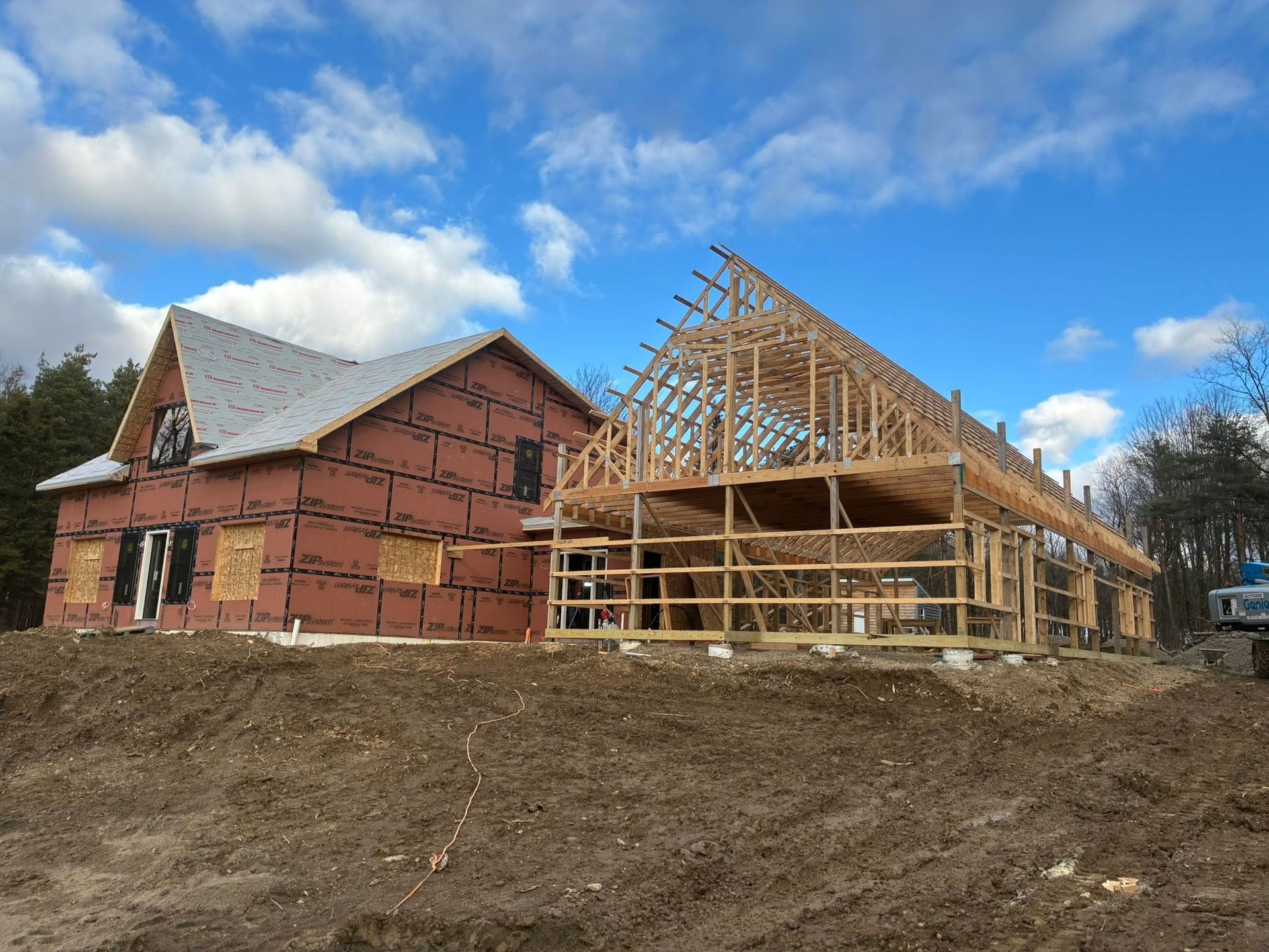 Partially built house with exposed wooden framing on a sloped lot under a blue sky