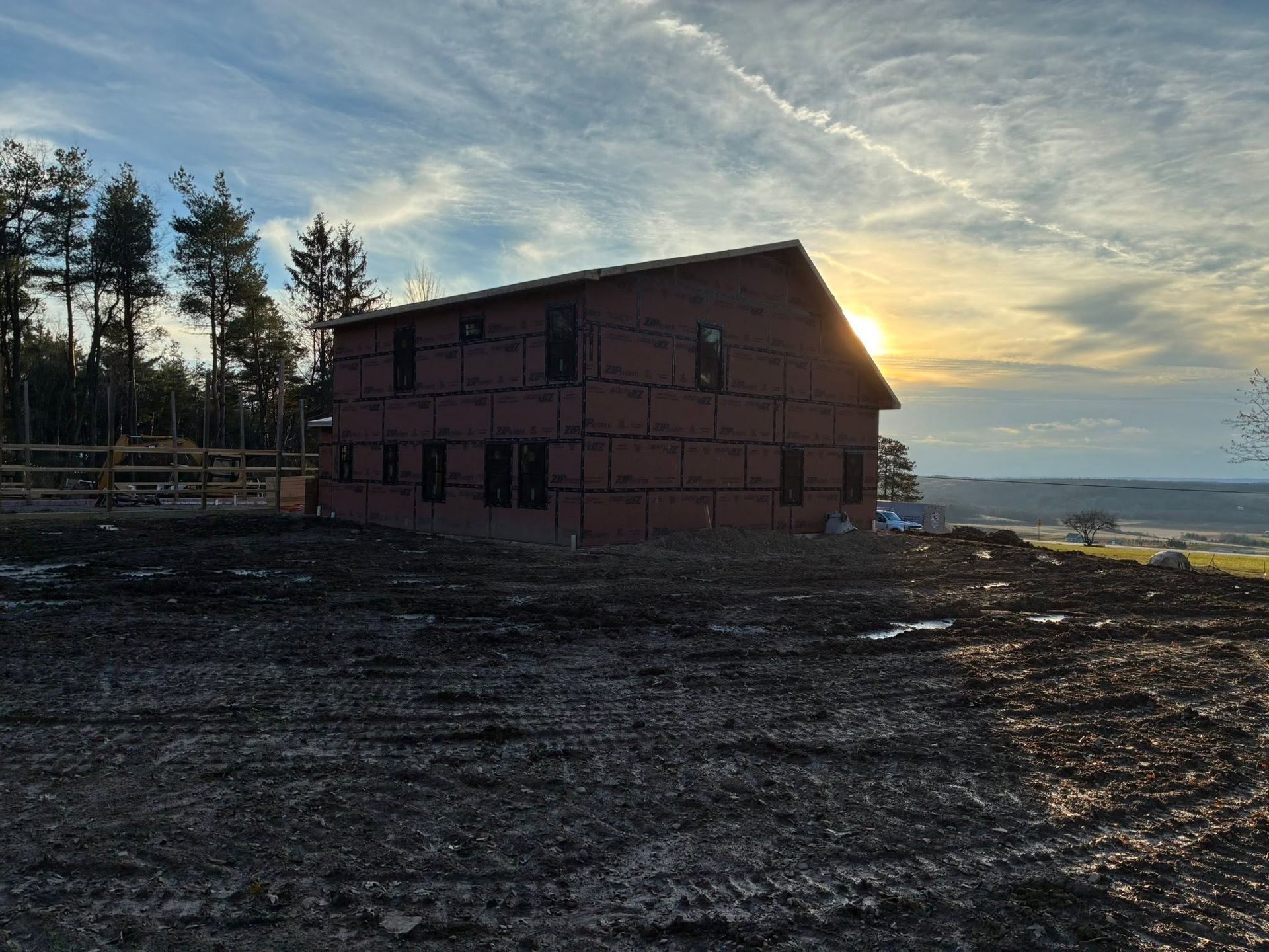 A red wooden house on a rocky beach at sunset, with trees and ocean in the background.