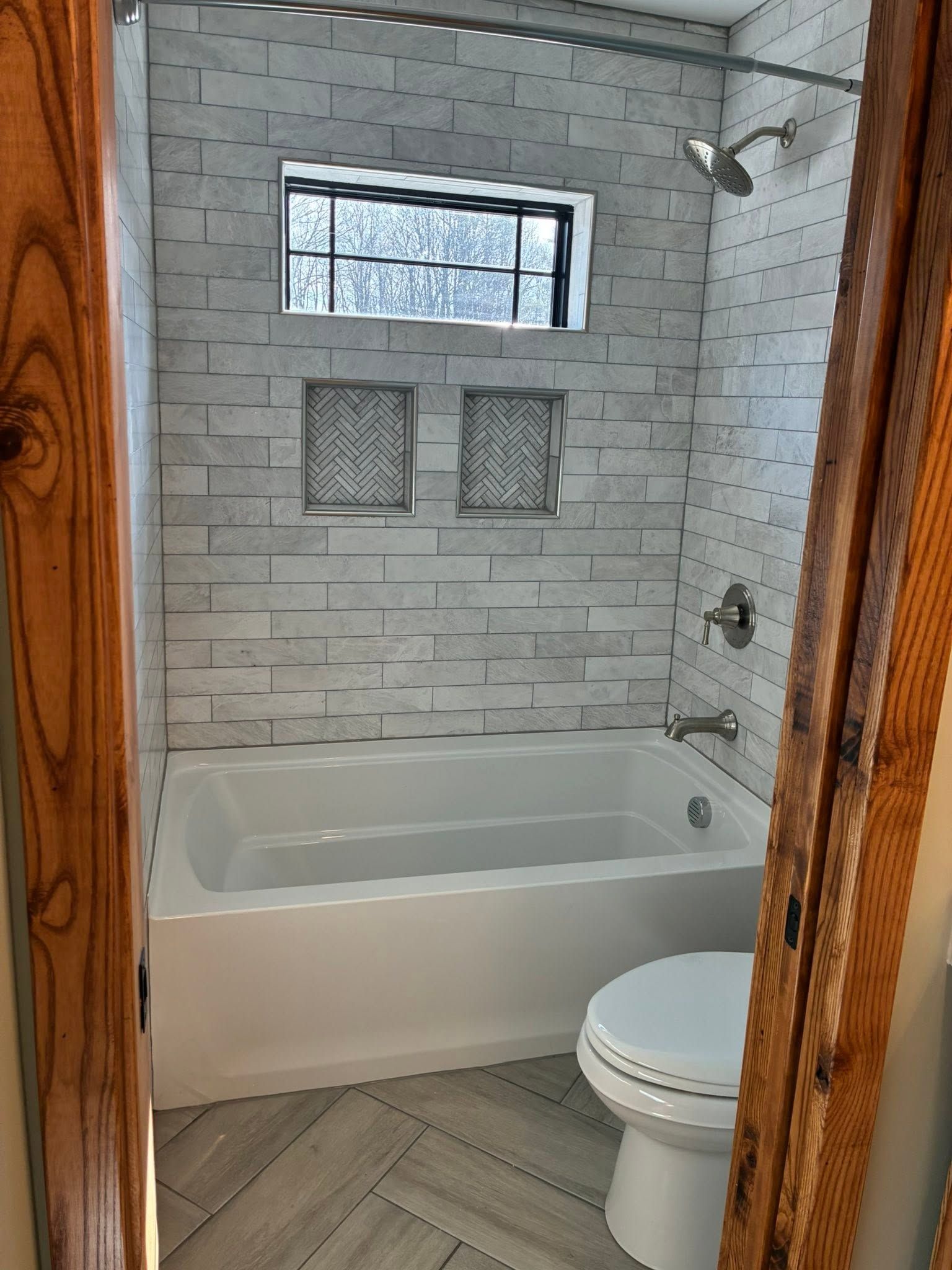 Small bathroom with a bathtub, toilet, tiled walls, and two frosted window niches.