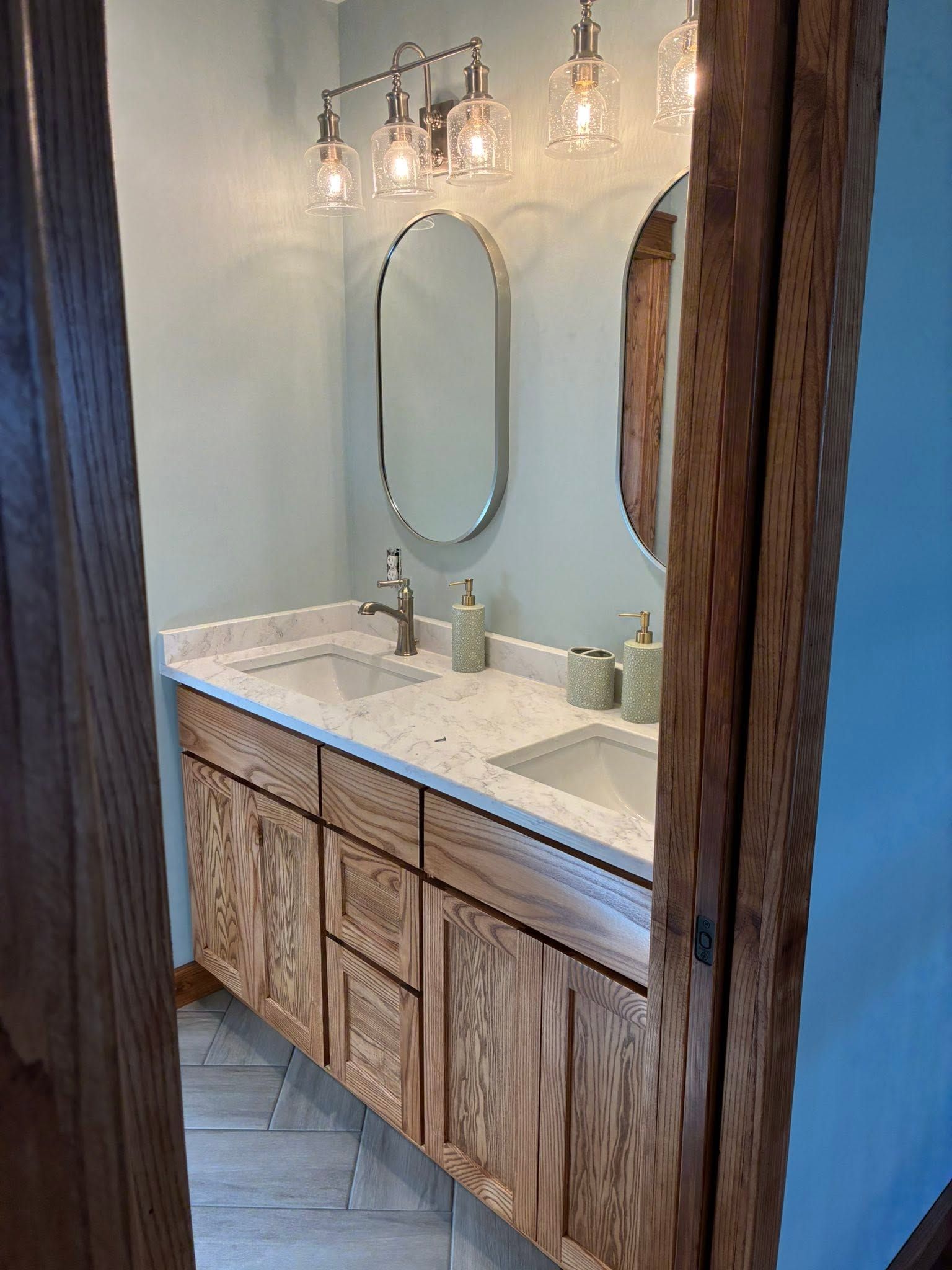 Rustic bathroom vanity with marble countertop, oval mirror, and wall sconces in a narrow alcove