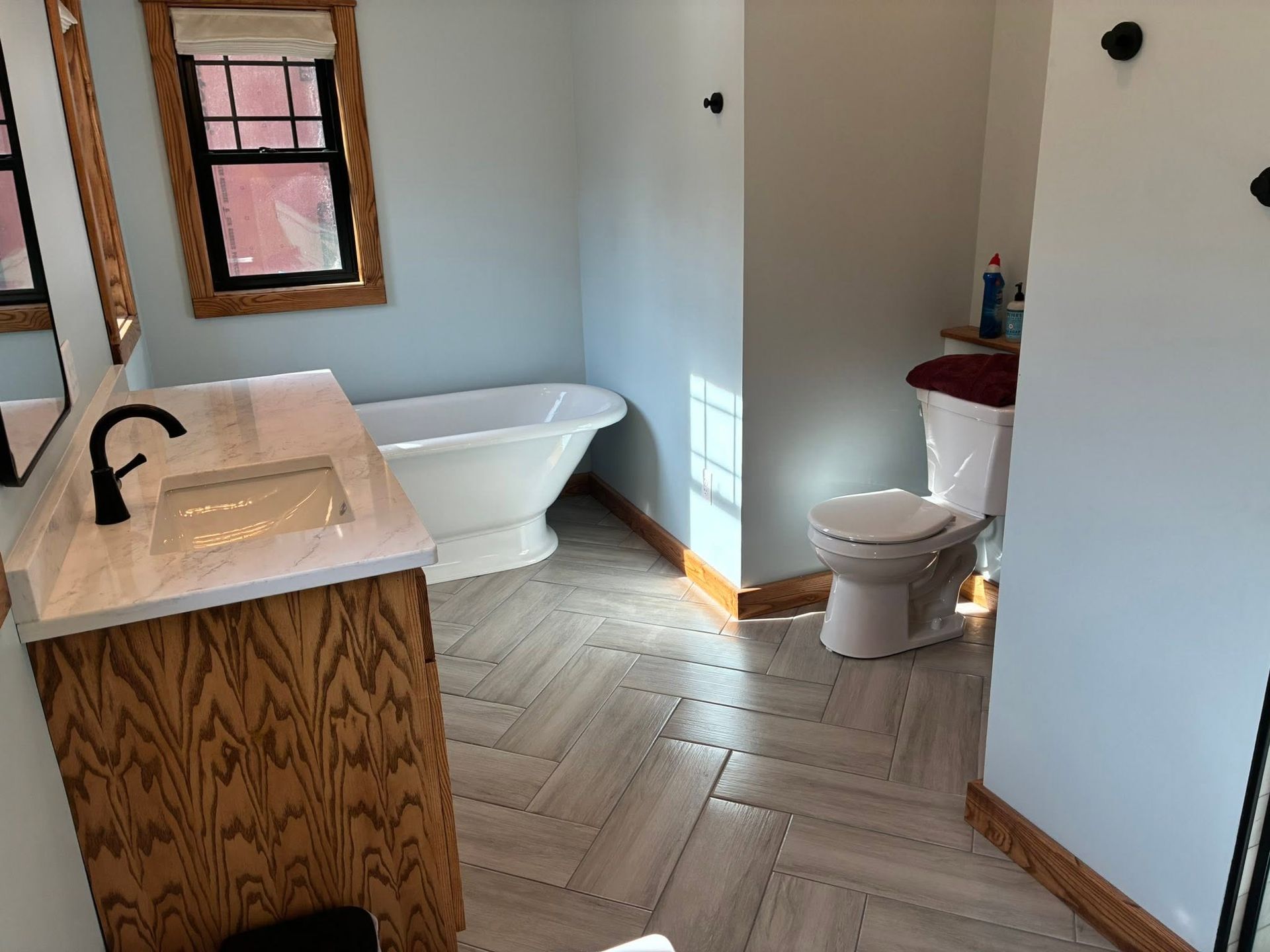 Modern bathroom with a freestanding tub, wood vanity, and herringbone tile floor.