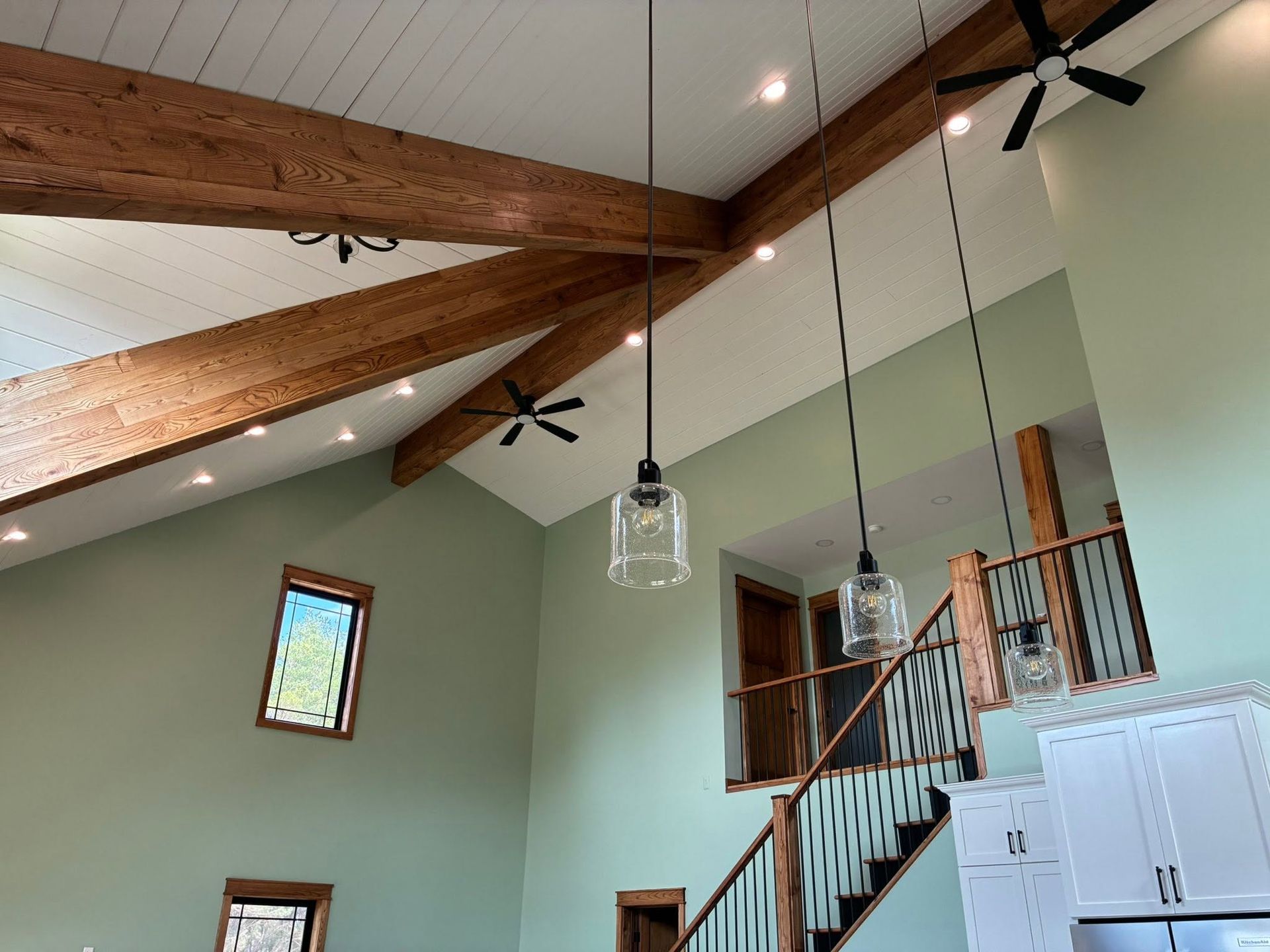 High vaulted kitchen with exposed wood beams, ceiling fans, and hanging pendant lights above white cabinets.