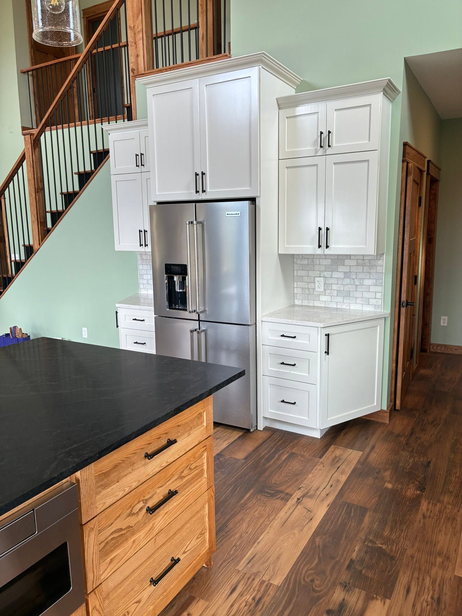 Modern kitchen with stainless steel fridge, white cabinets, black island, and wood floors