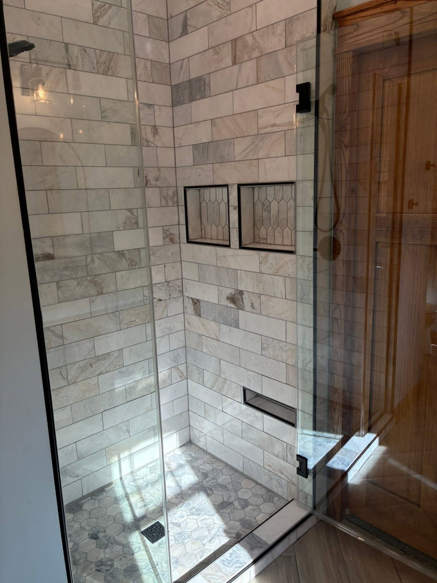 Glass shower with white subway tile and wooden door panel