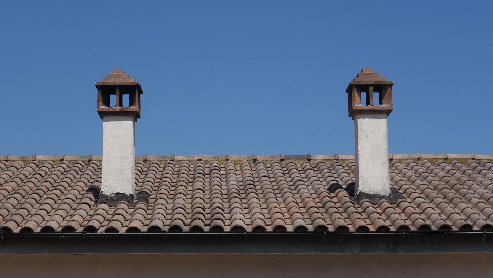 Two white chimneys with brown tops on a tiled roof under a blue sky.