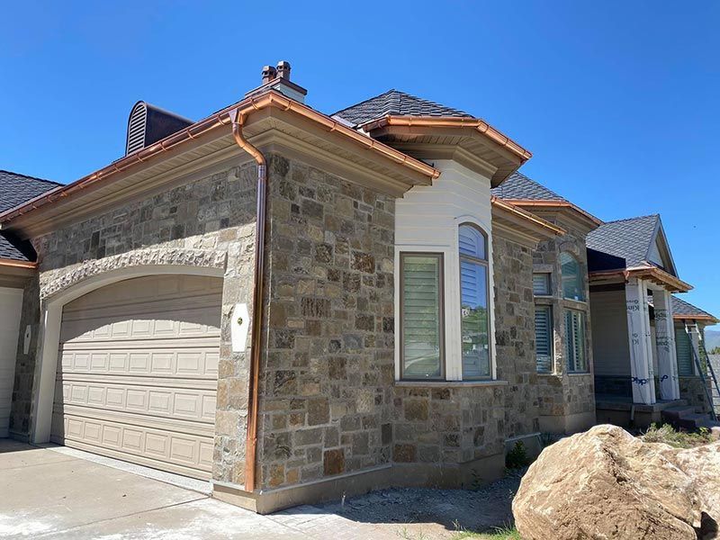 Stone-front suburban house with beige garage and blue roof under a clear sky