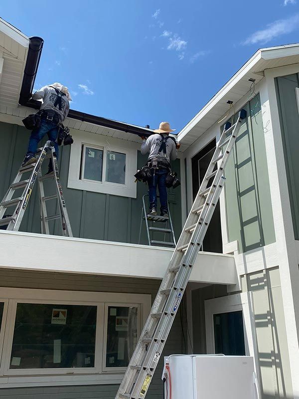 Two workers on ladders painting a gray two-story house exterior