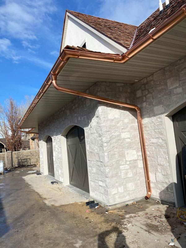Stone building exterior with copper gutters, arched doorways, and blue sky above.