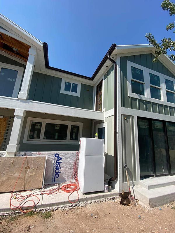 Exterior of a modern house under construction with white siding, large windows, and exposed materials in front
