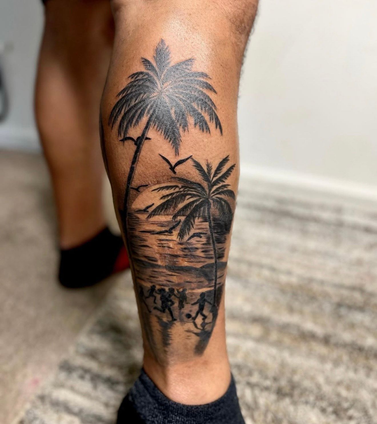 A person has a tattoo of palm trees on their leg.