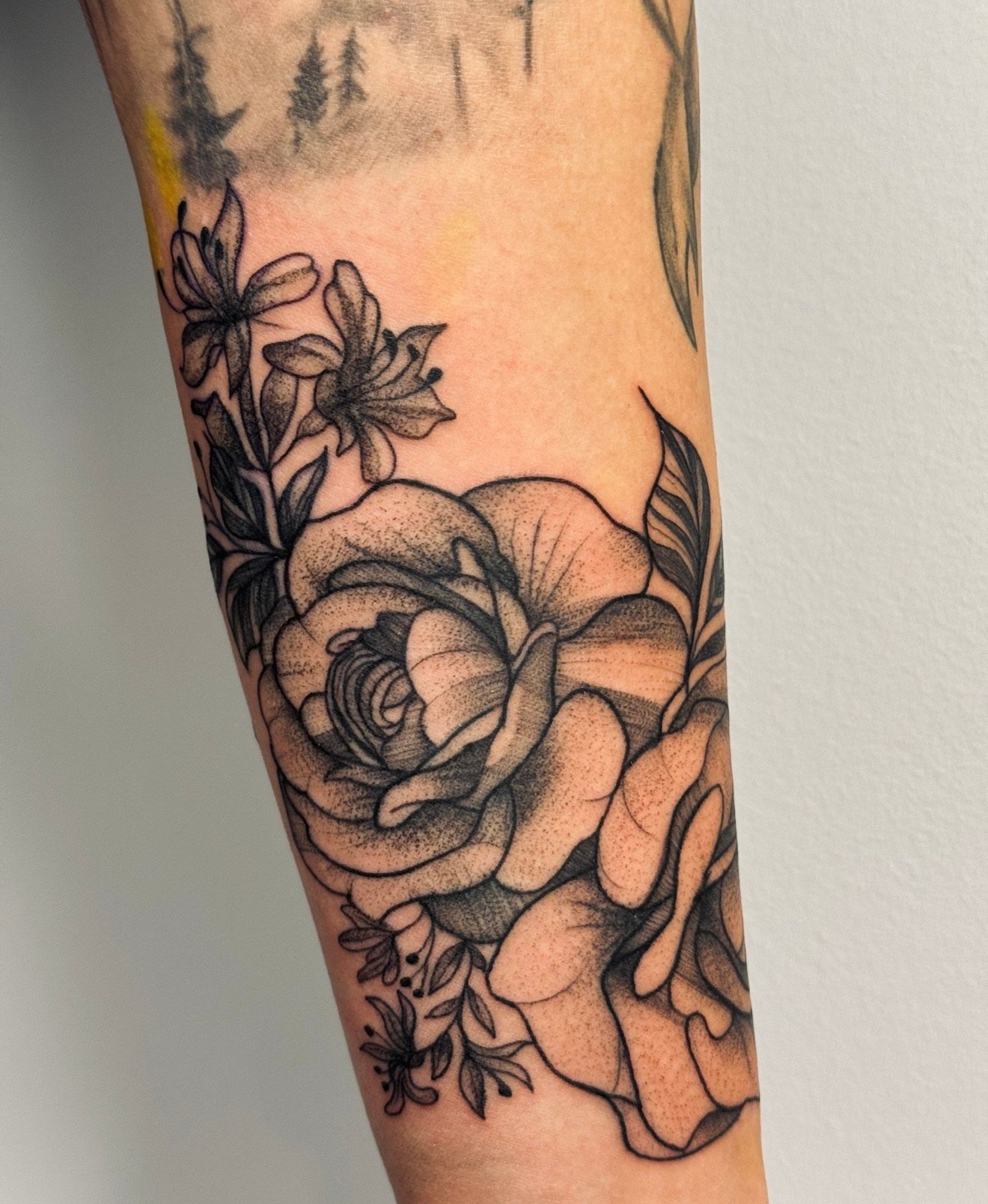 A person has a tattoo of roses and leaves on their forearm.