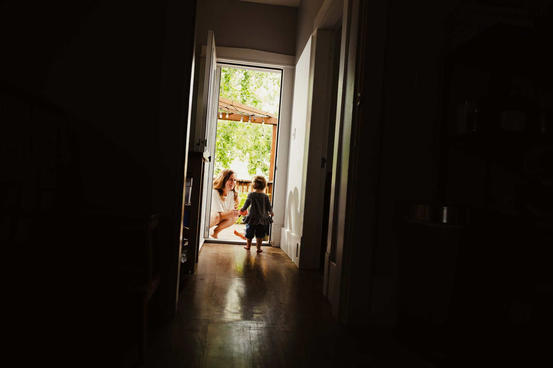 Two people sitting at a bright doorway at the end of a dark hallway