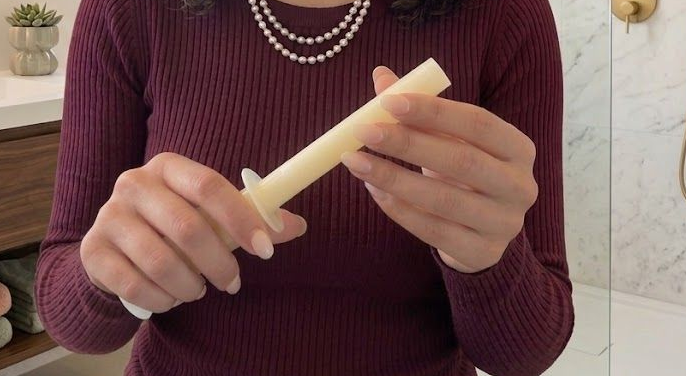 Person in a burgundy sweater holding a cream-colored cylindrical candle indoors