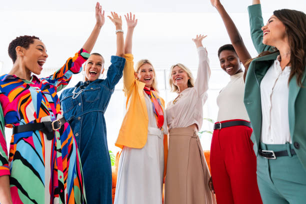 A group of people in colorful clothes cheering with arms raised in a bright indoor setting