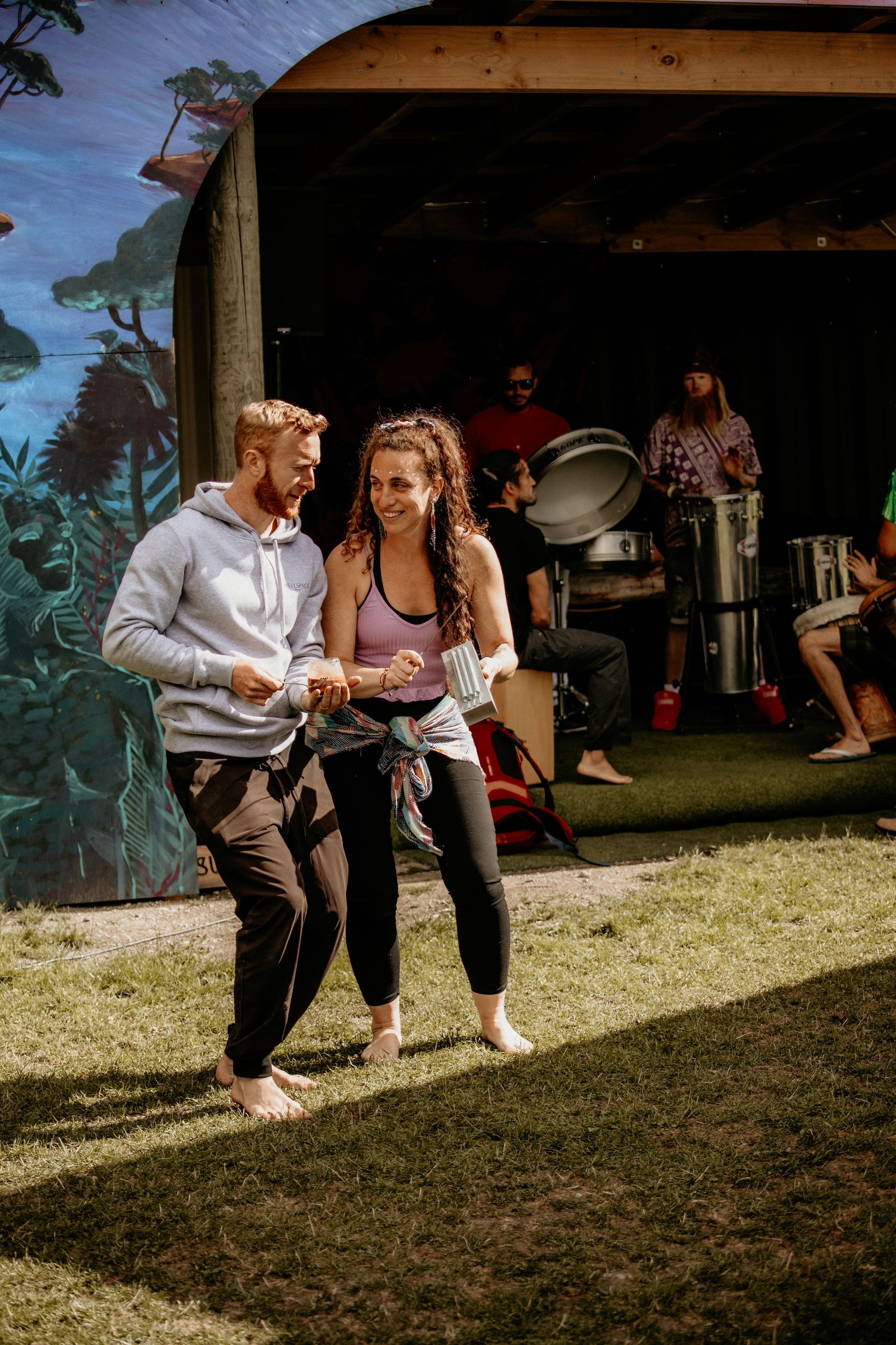 Couple dancing barefoot outdoors with band playing under awning.