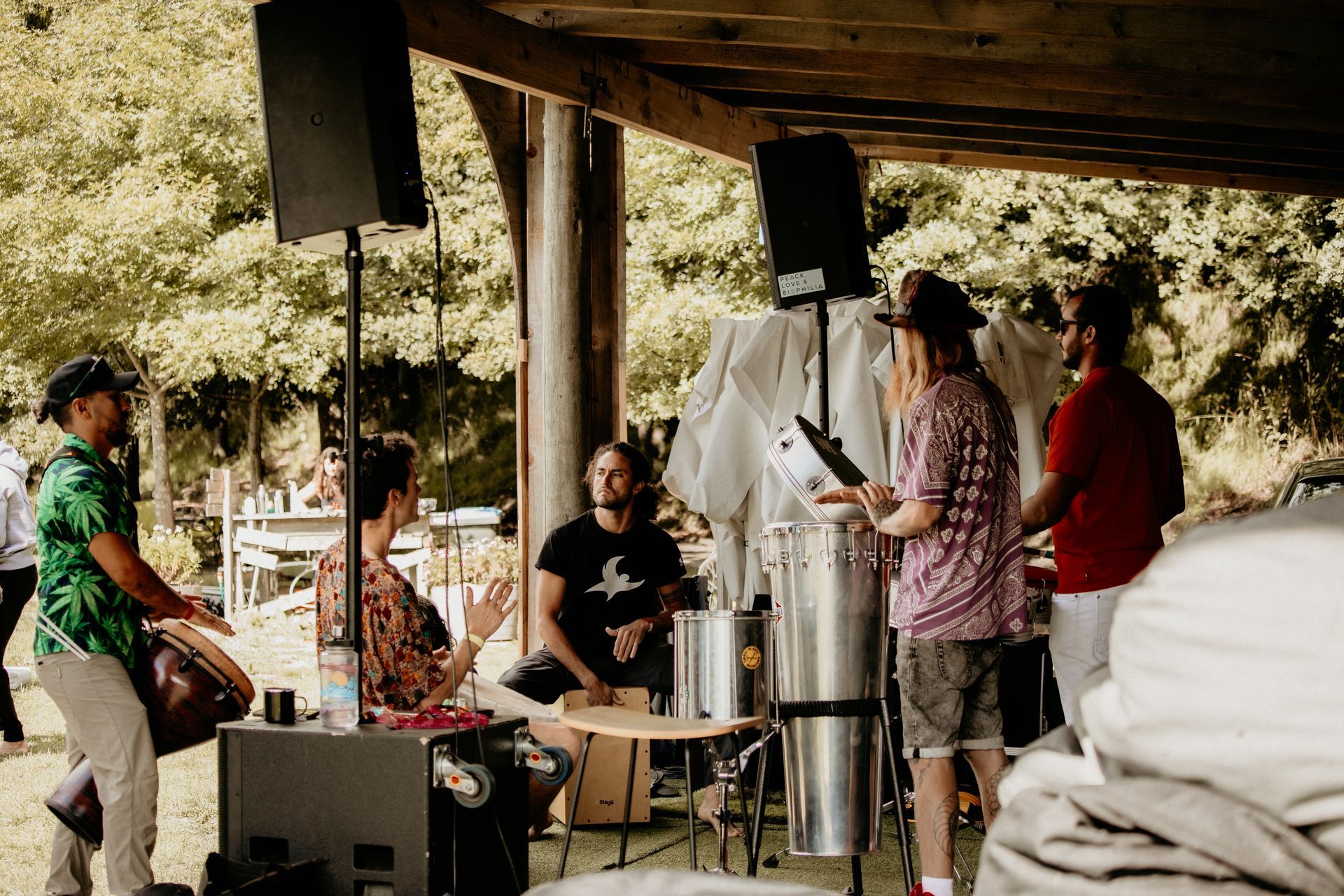 Band performing outdoors under a wooden structure. Musicians playing drums and percussion instruments.