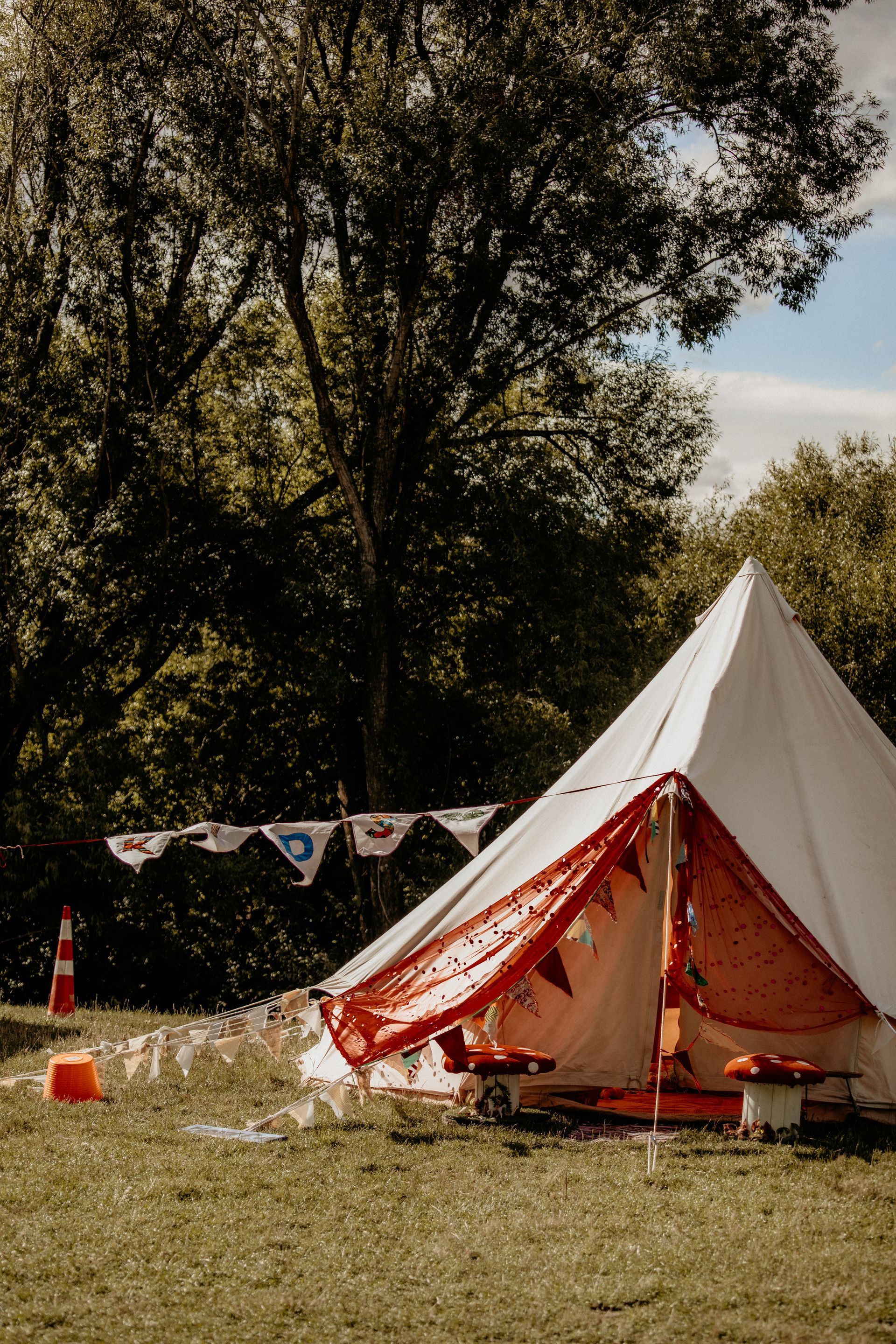 White tent decorated with red bunting sits on a green lawn with a tree in the background.