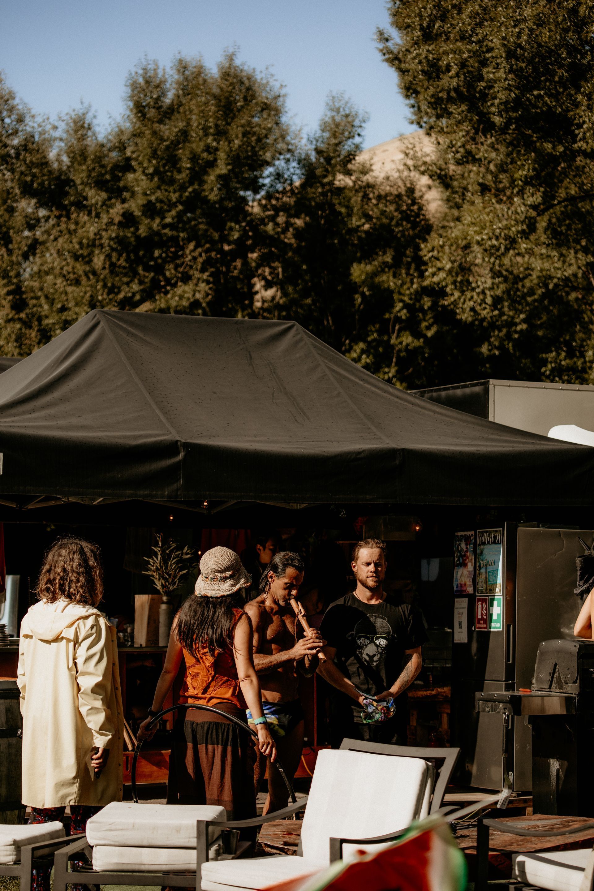 People gather at a black canopy tent in a sunny outdoor setting.
