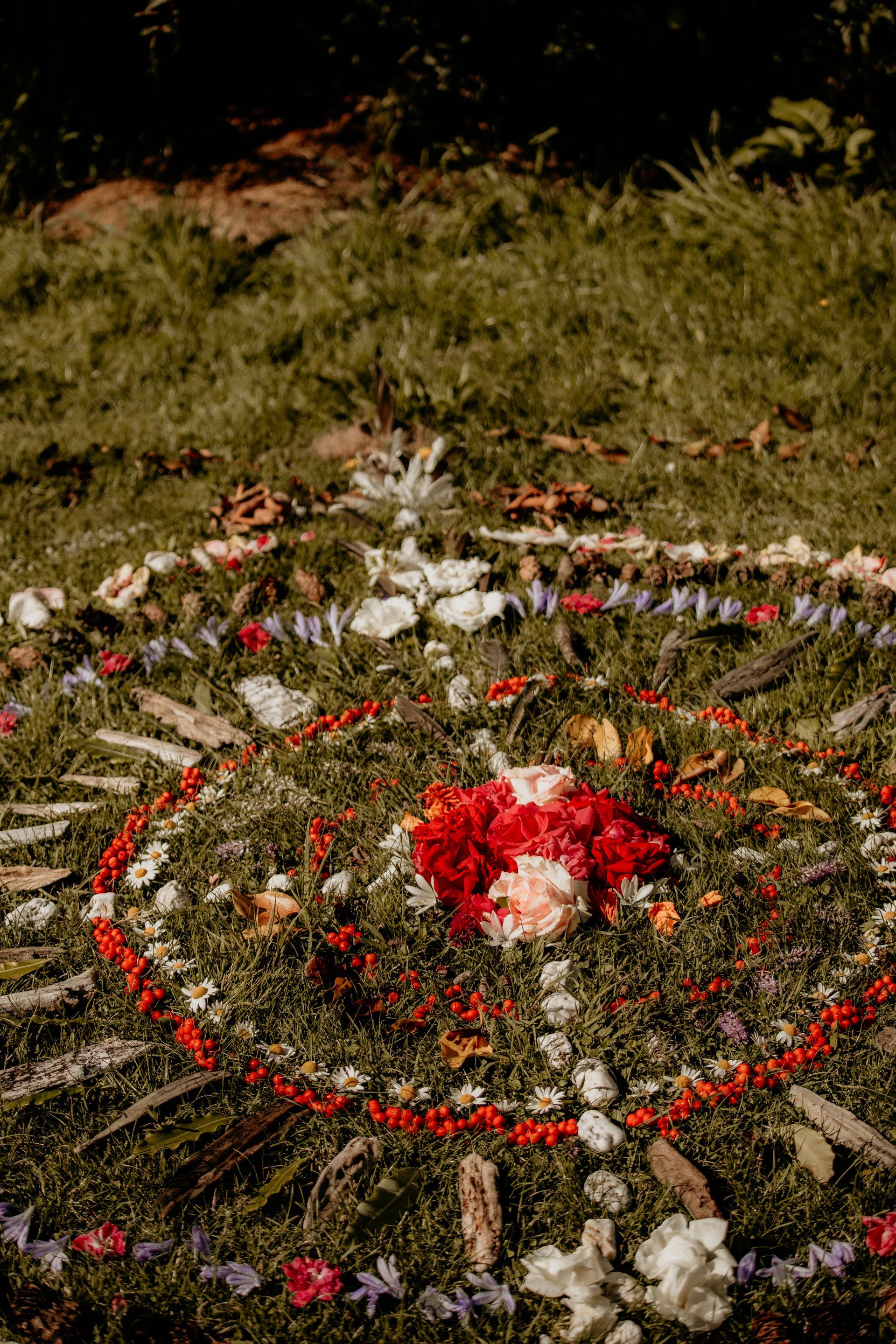 A floral mandala on green grass. Red, white, and orange flowers arranged in a circular design.