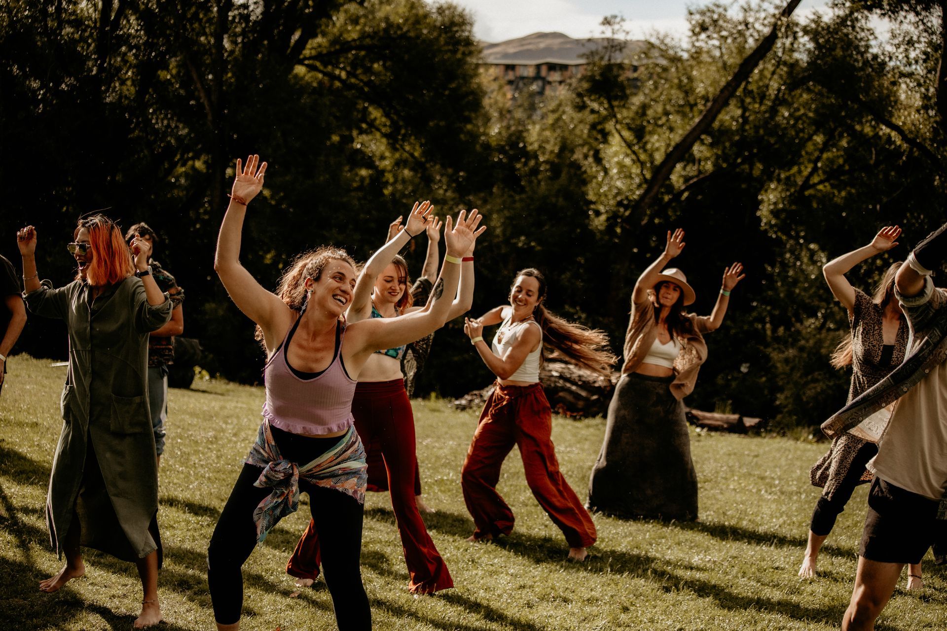 People dancing joyfully outdoors in a sunny park with arms raised.